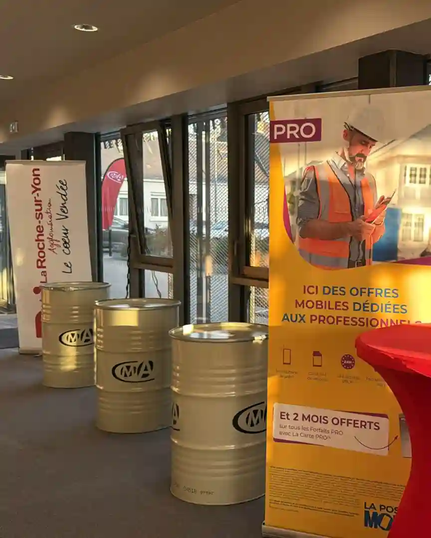 Espace d'accueil avec tonneaux décoratifs logotypés CMA et kakémonos publicitaires de La Poste Mobile et La Roche-sur-Yon Agglomération.